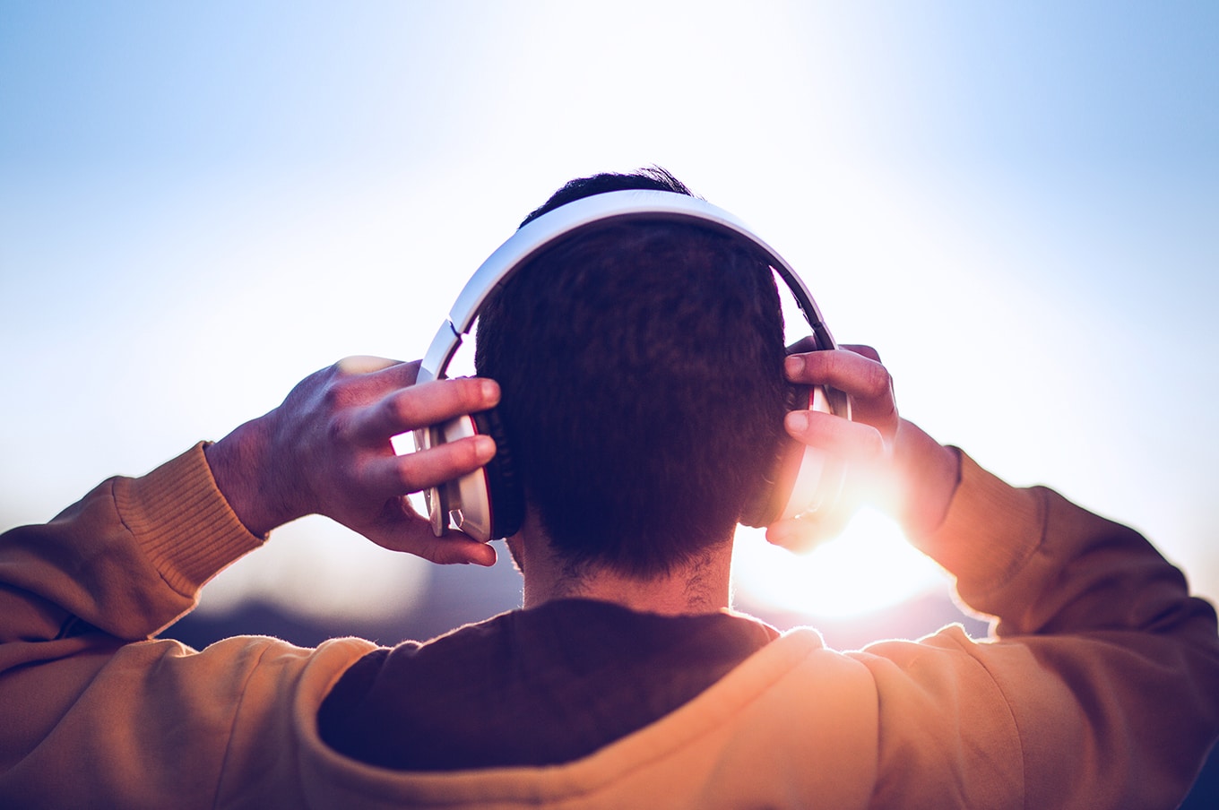 Person wearing over-ear headphones, viewed from behind in sunlight.