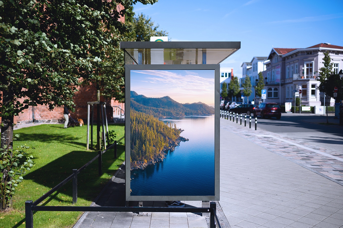 Digital out of home advertising display at a city bus stop, showing a full screen landscape image along a pedestrian street.