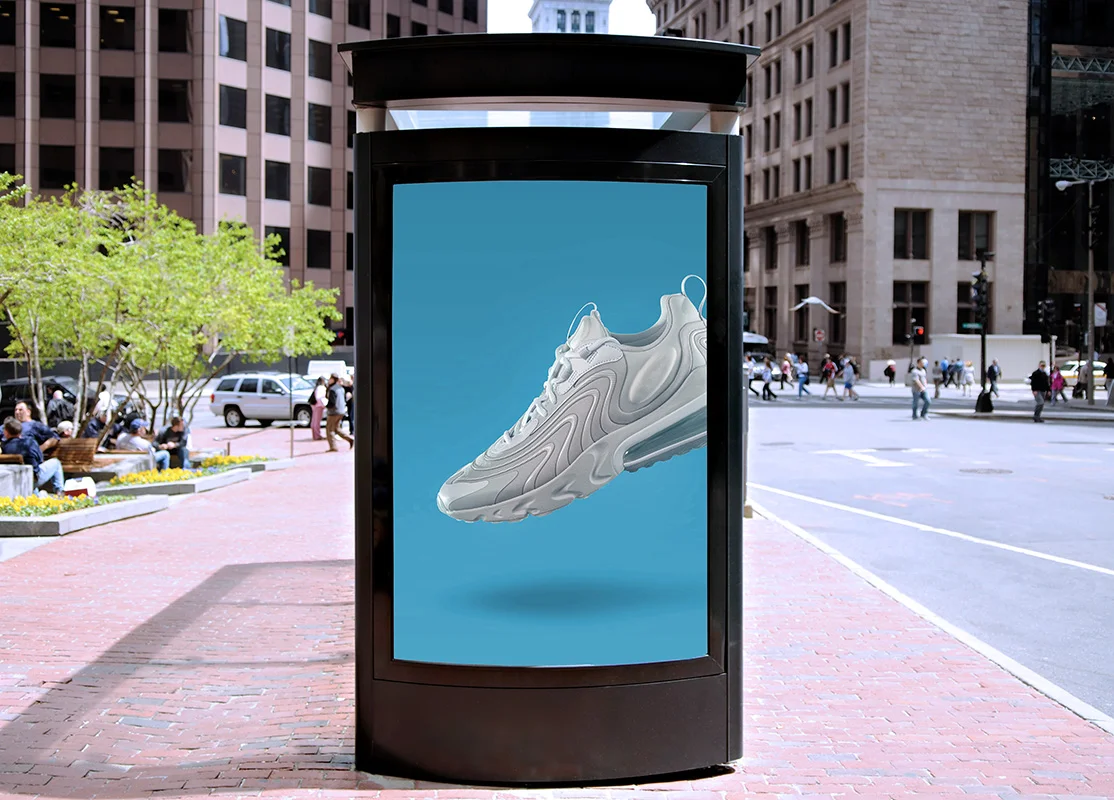 Digital out of home advertising display on a city sidewalk, featuring a product advertisement in an urban business district.